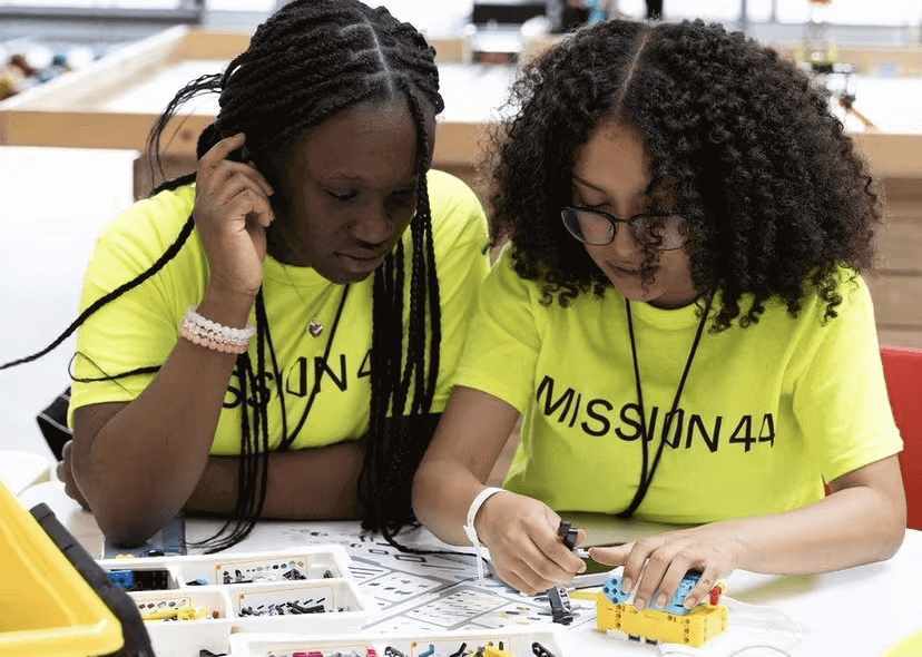 Two young girls in neon shirts engaged in a hands-on STEM activity, collaborating on a project with colorful building pieces.
