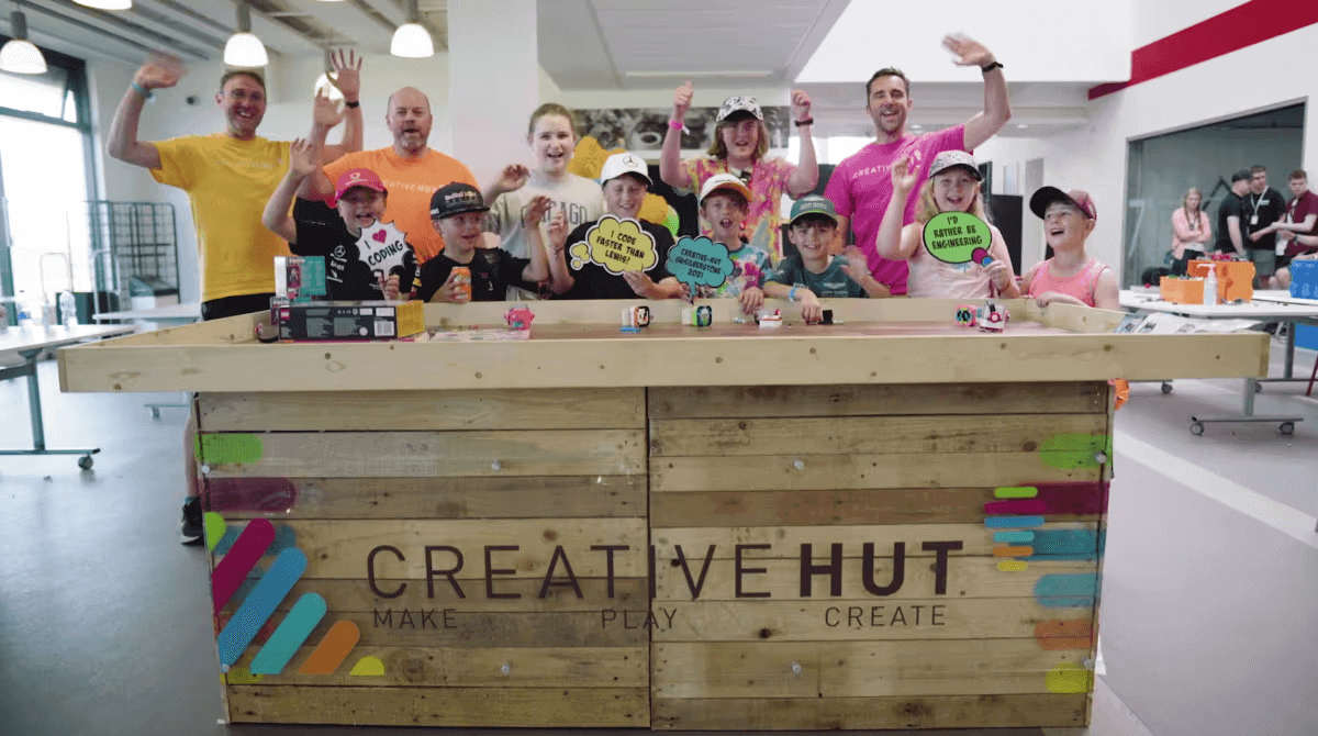 Group of children and adults enjoying an edutainment experience at Creative Hut, smiling and waving in a vibrant workshop.