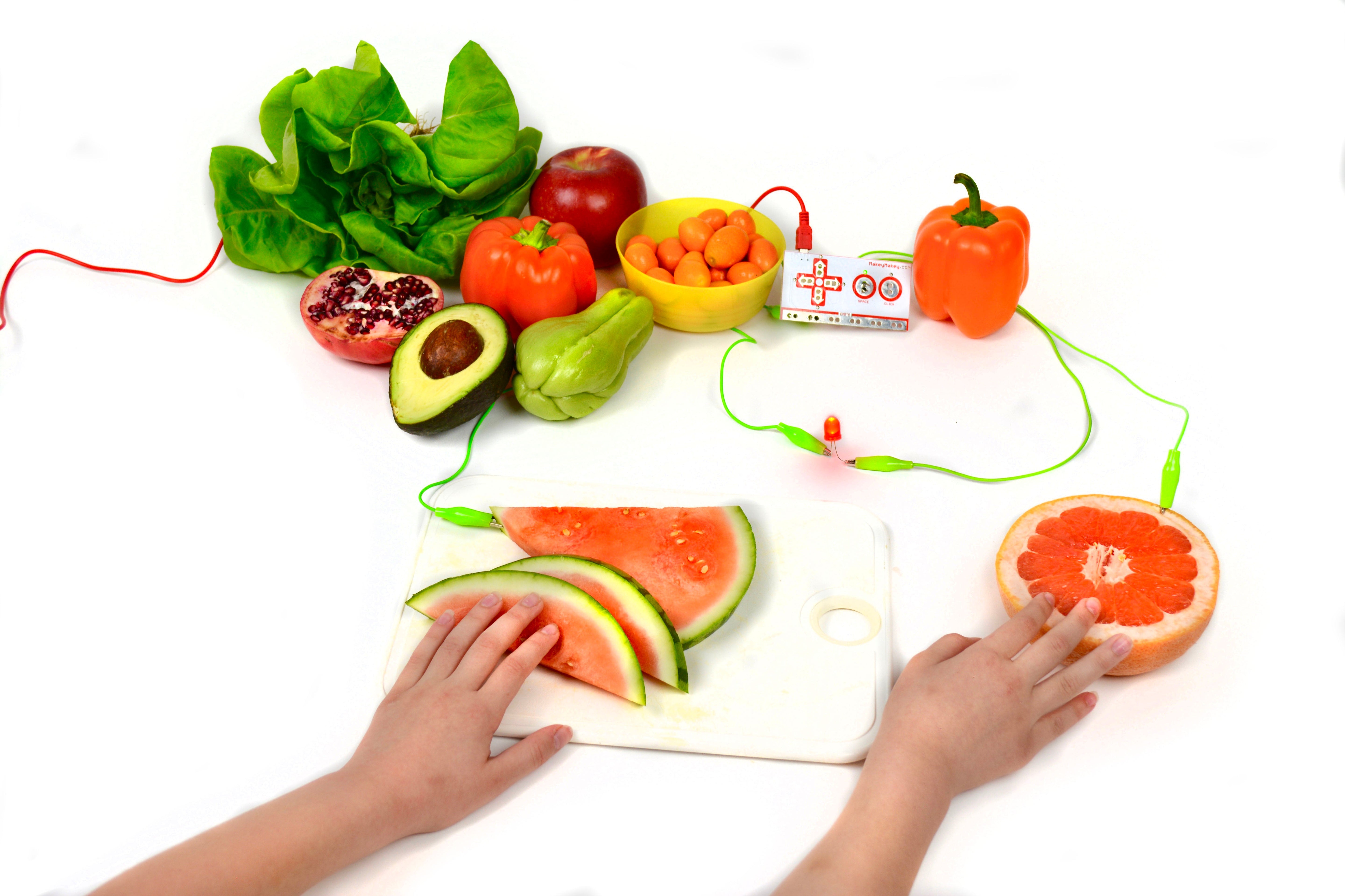 Child's hands touching interactive fruits and vegetables with wires, illustrating a fun learning activity about healthy eating.