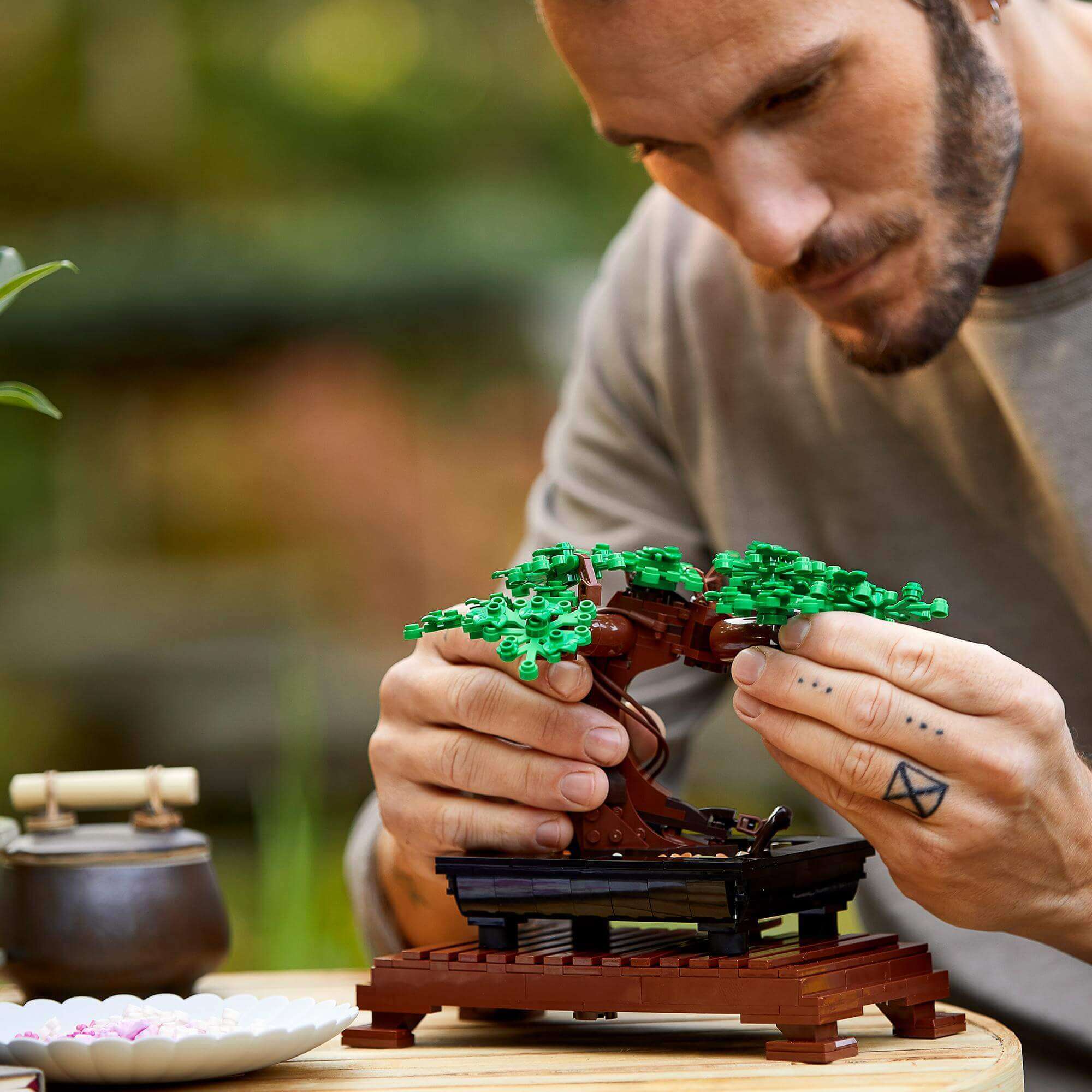 Man building a LEGO® Bonsai Tree set, featuring interchangeable green leaves and pink cherry blossoms.
