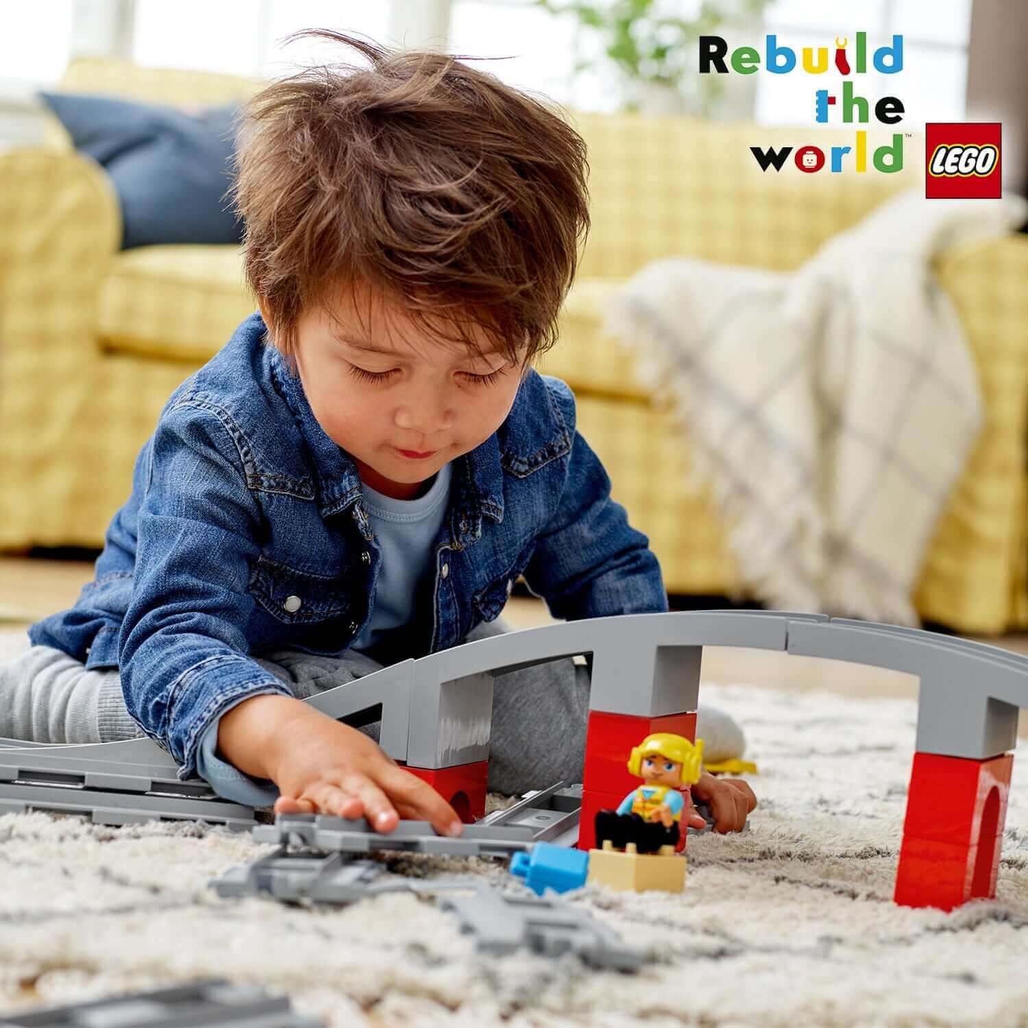 Child playing with LEGO® DUPLO Town Train Bridge and Tracks Set 10872, building colorful train tracks at home.