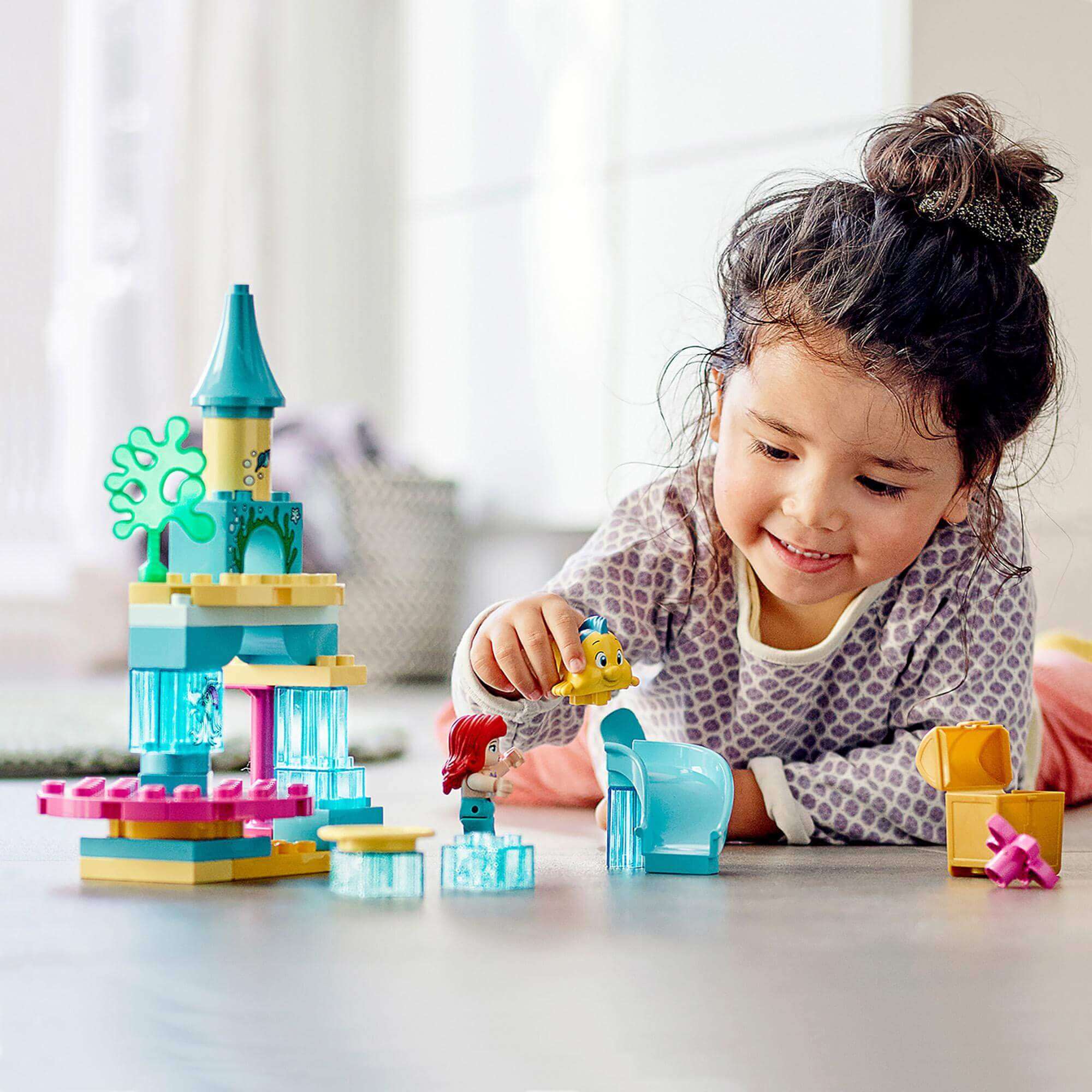 Child playing with LEGO® DUPLO Princess Ariel Undersea Castle Set 10922, featuring Ariel and Flounder characters.