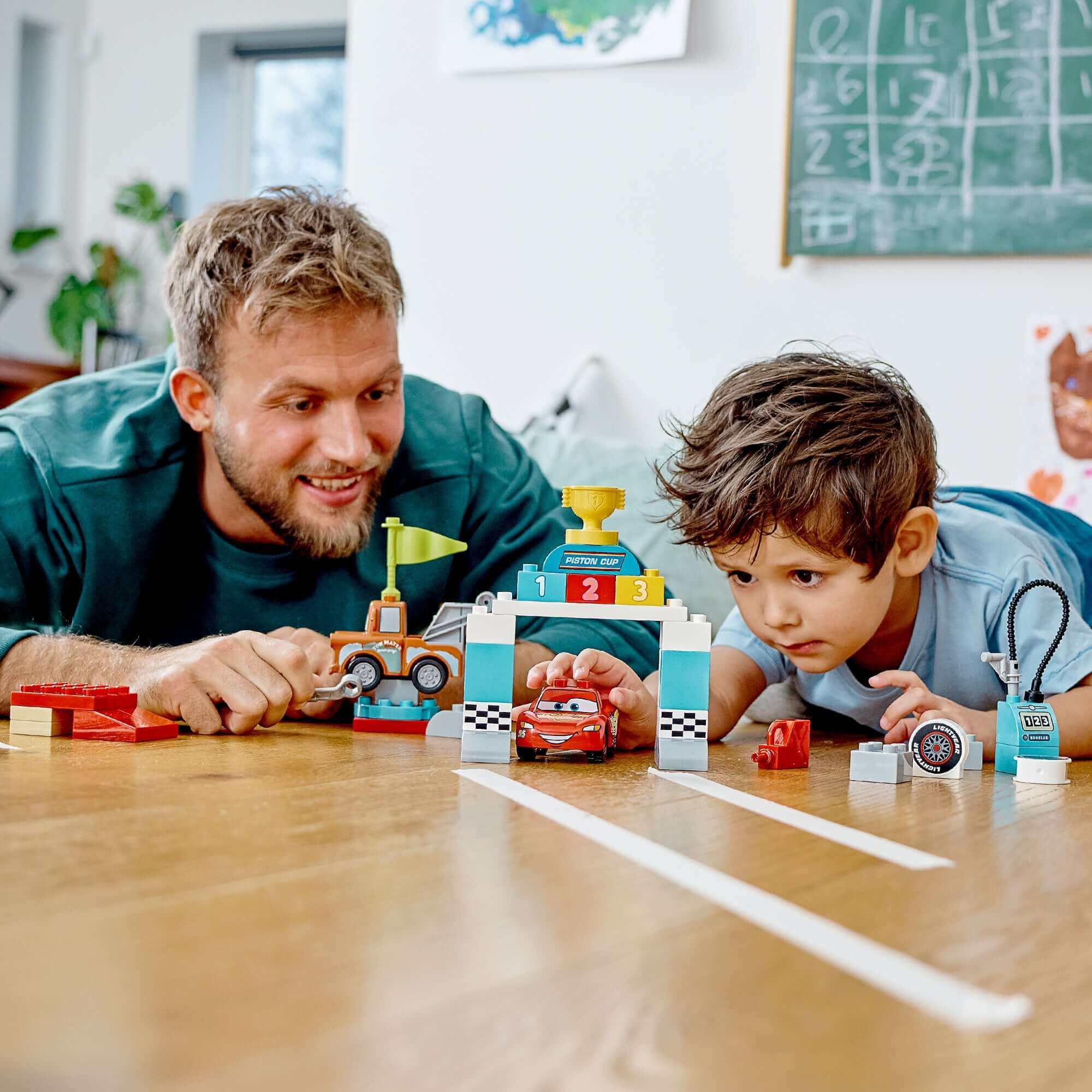 Dad and son playing with LEGO DUPLO Cars Lightning McQueen Race Day set, enhancing fine motor skills through imaginative play.