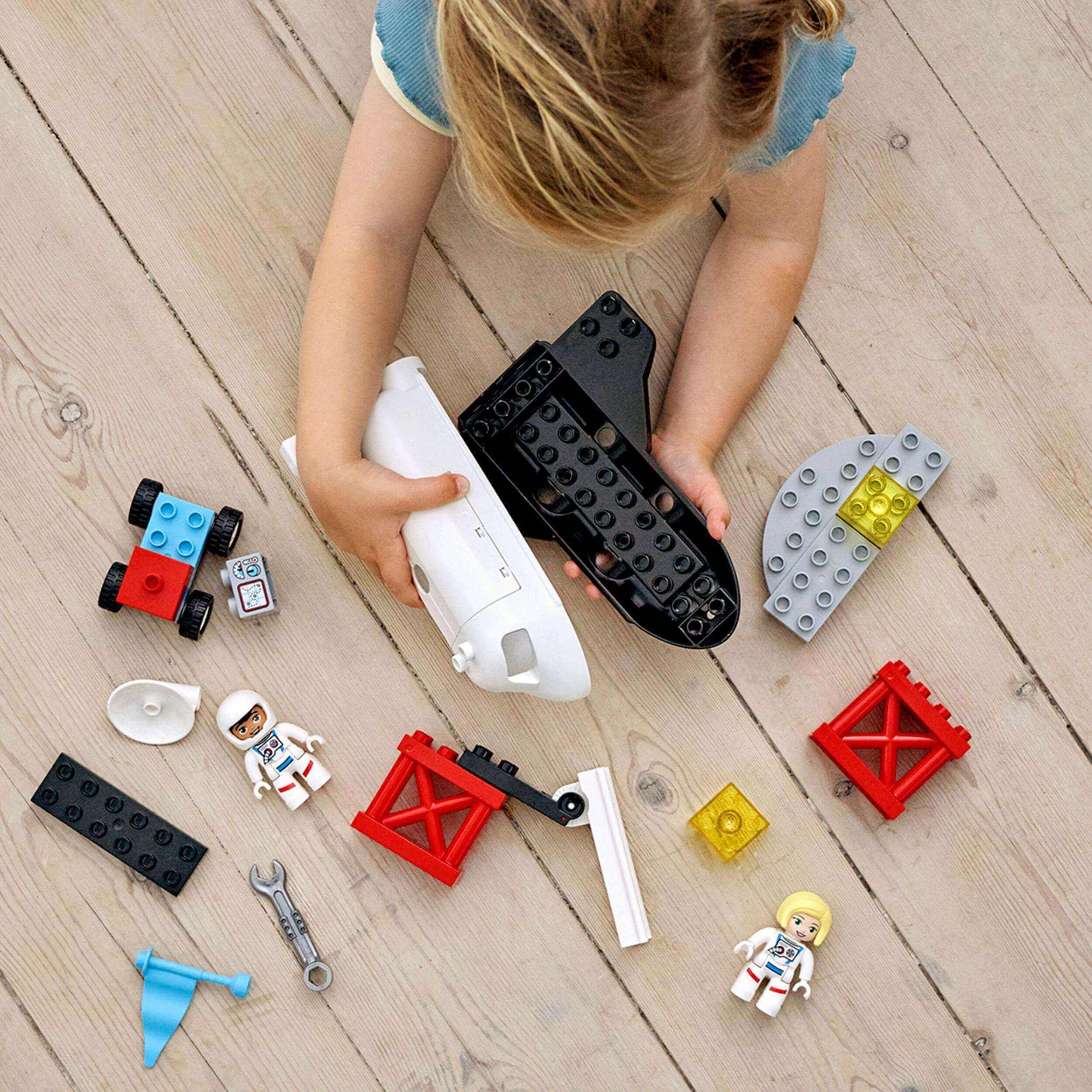 Child playing with LEGO® DUPLO Space Shuttle Mission set, featuring shuttle, astronauts, and colorful building pieces.