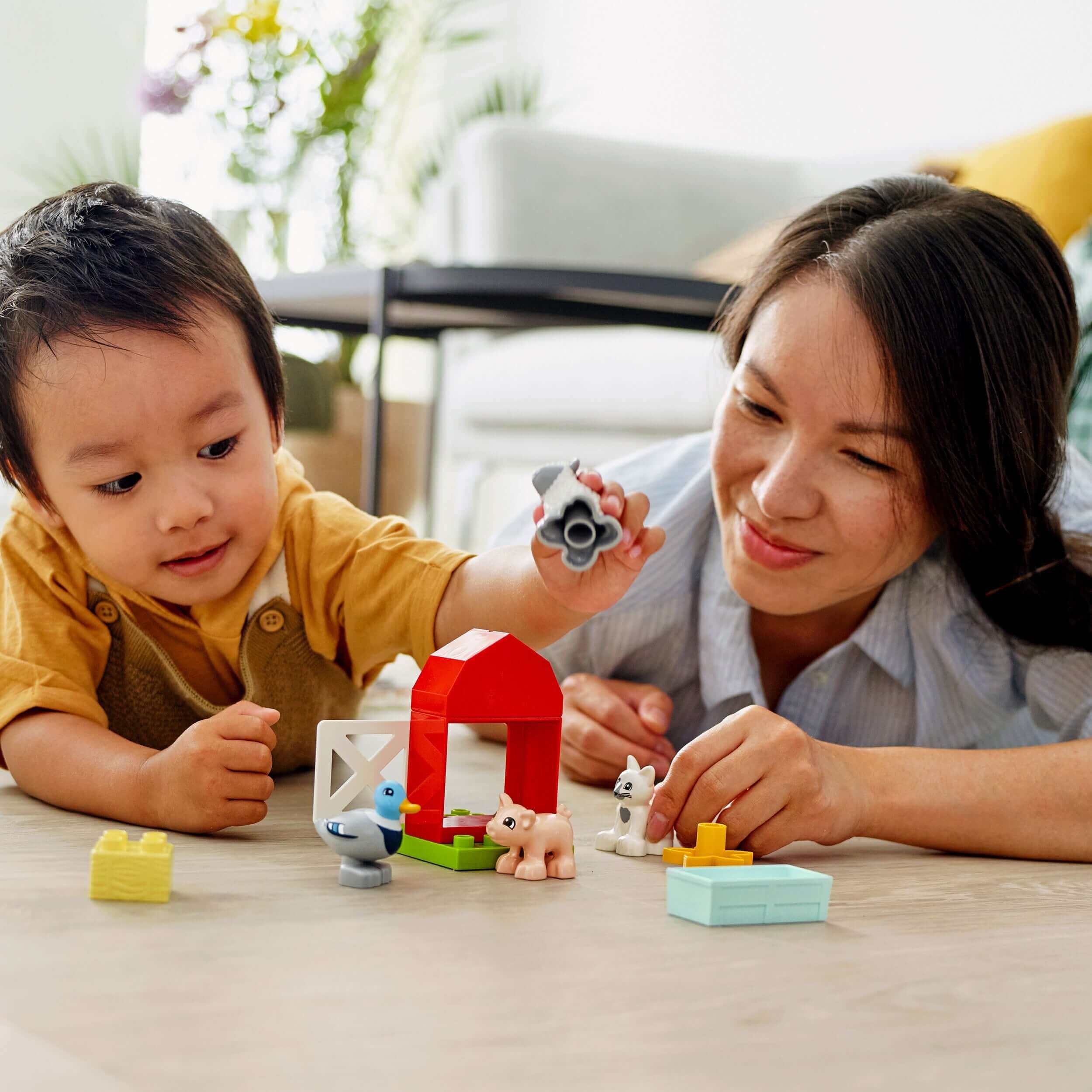 Toddler playing with LEGO DUPLO Town Farm Animal Care set, engaging with farm animals and mother guiding creative play.