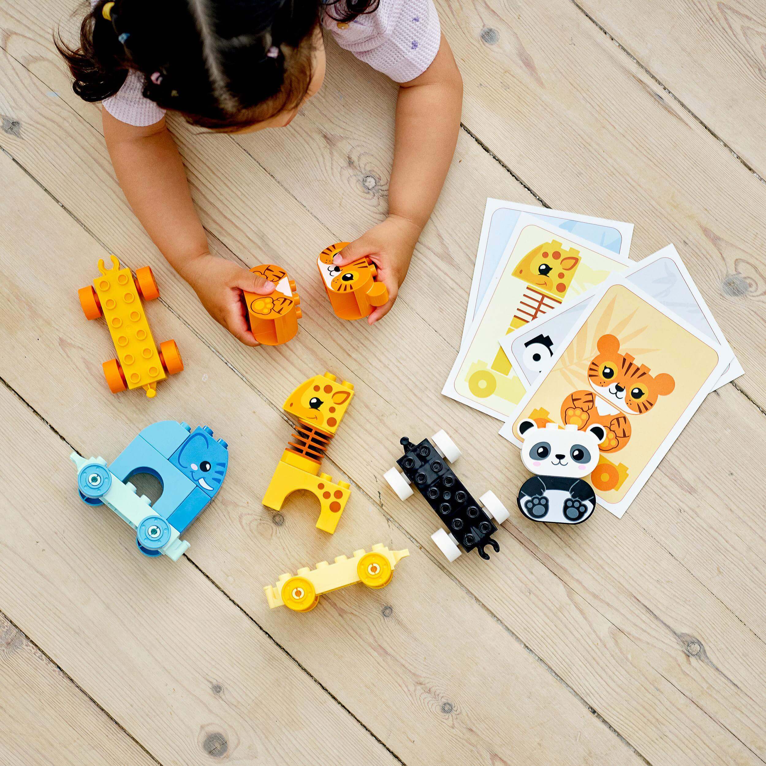Child playing with LEGO DUPLO Animal Train, featuring colorful animal blocks and cards on a wooden floor.