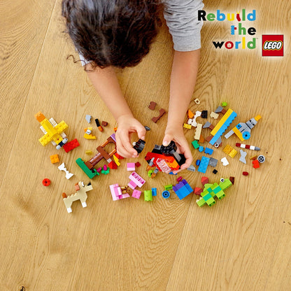 Child playing with LEGO® Classic Basic Brick Set 11002, creating with colorful bricks on wooden floor.