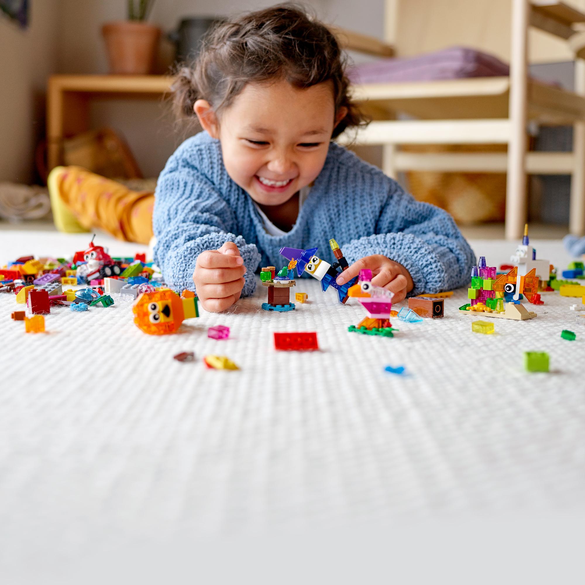 A happy child playing on the floor with colorful LEGO® bricks and creative models, showcasing fun and imagination.