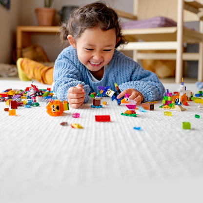 A happy child playing on the floor with colorful LEGO® bricks and creative models, showcasing fun and imagination.