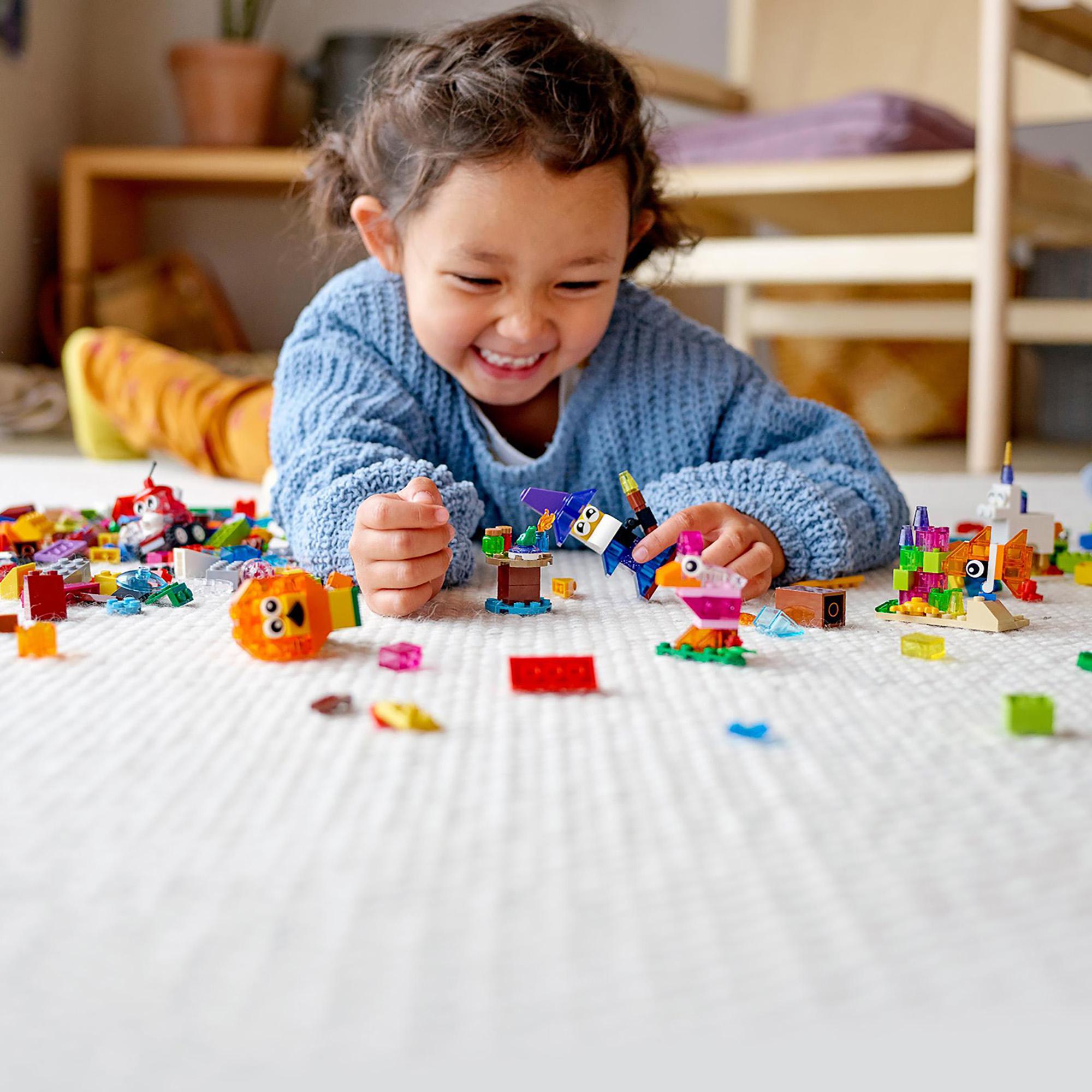 A happy child playing with colorful LEGO® pieces on the floor, showcasing creativity with transparent bricks from LEGO® Classic.