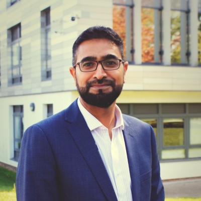 Businessman in a suit stands outdoors in front of a modern building, smiling and confident.