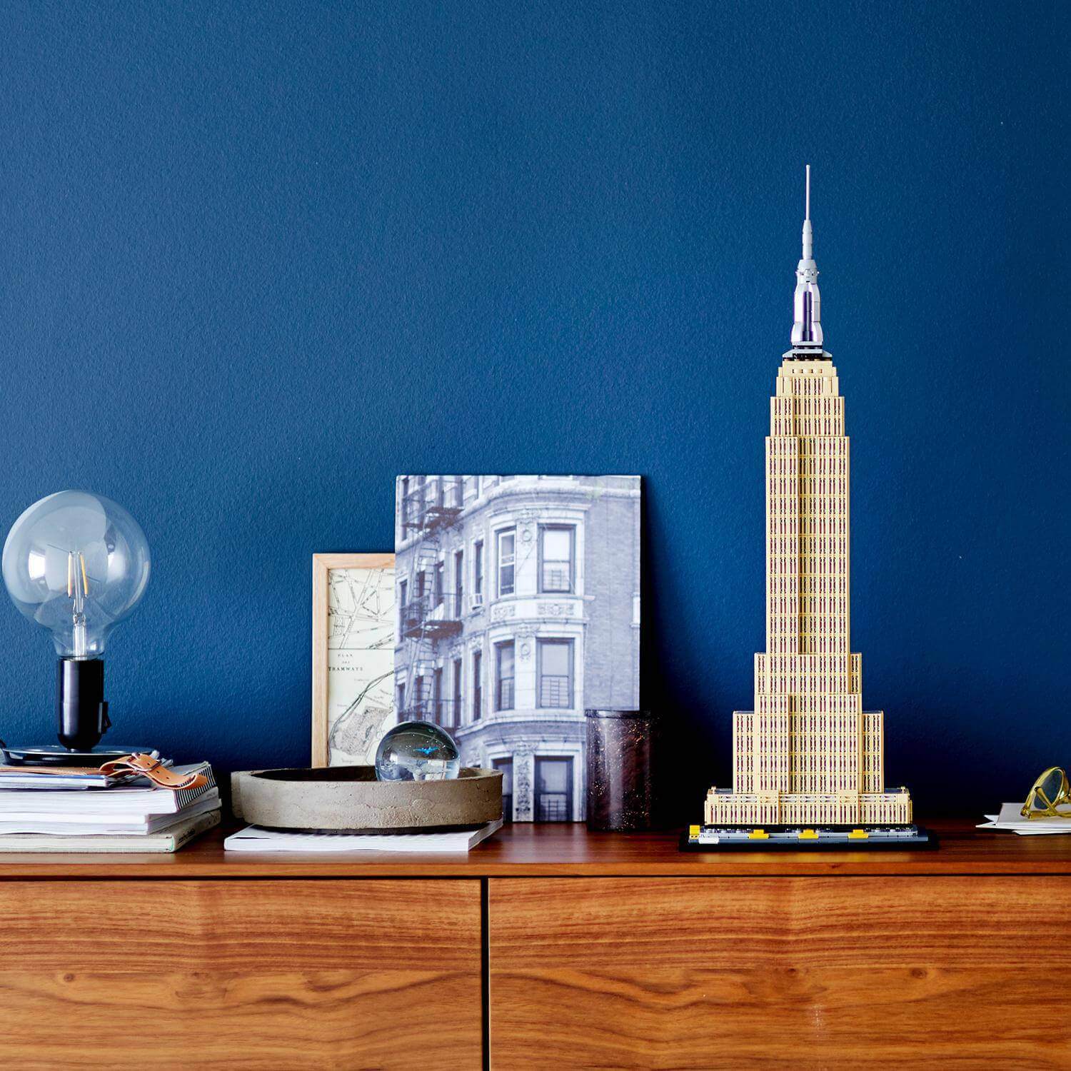 LEGO Architecture Empire State Building set displayed on a wooden shelf with decorative items and blue wall background.