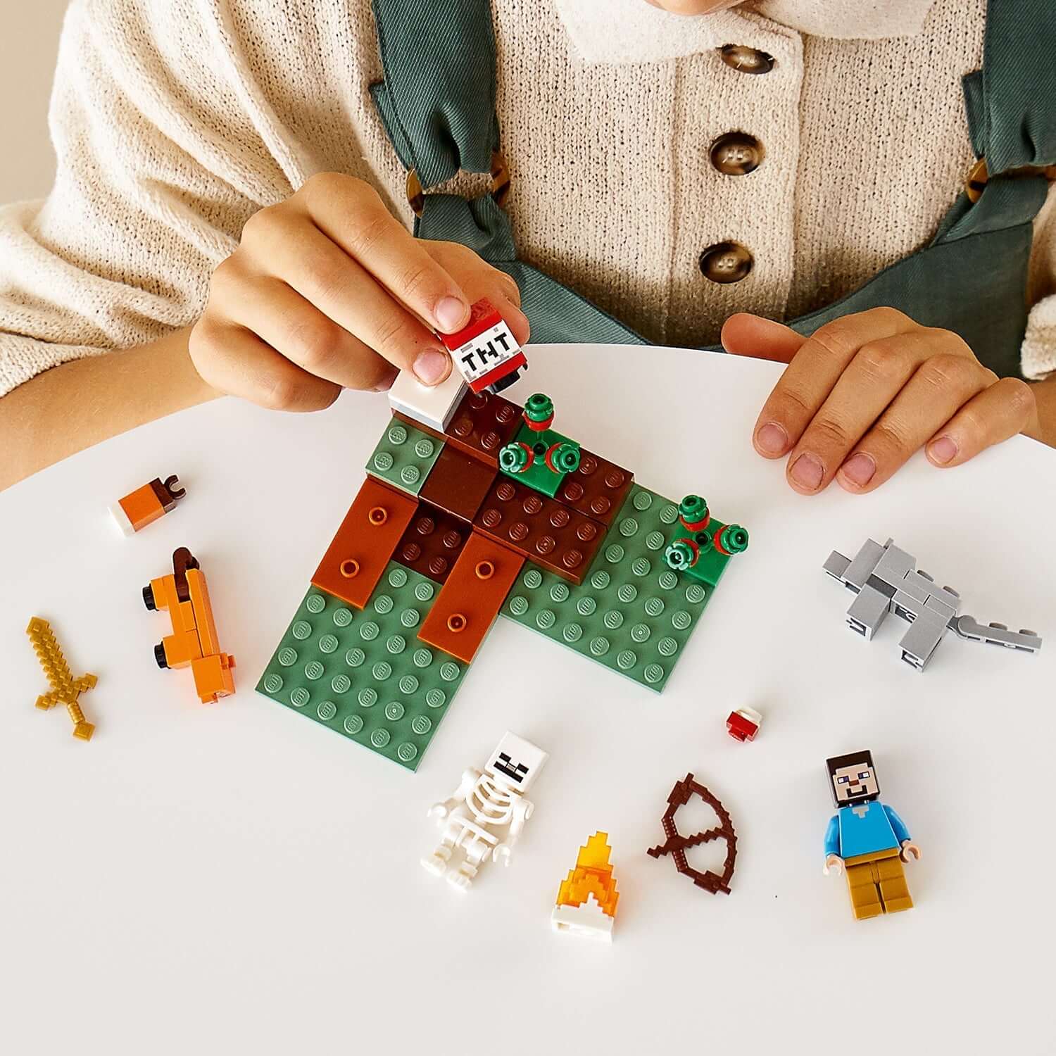 Child building with LEGO® Minecraft Taiga Adventure Set 21162, featuring characters, TNT, and mining accessories.