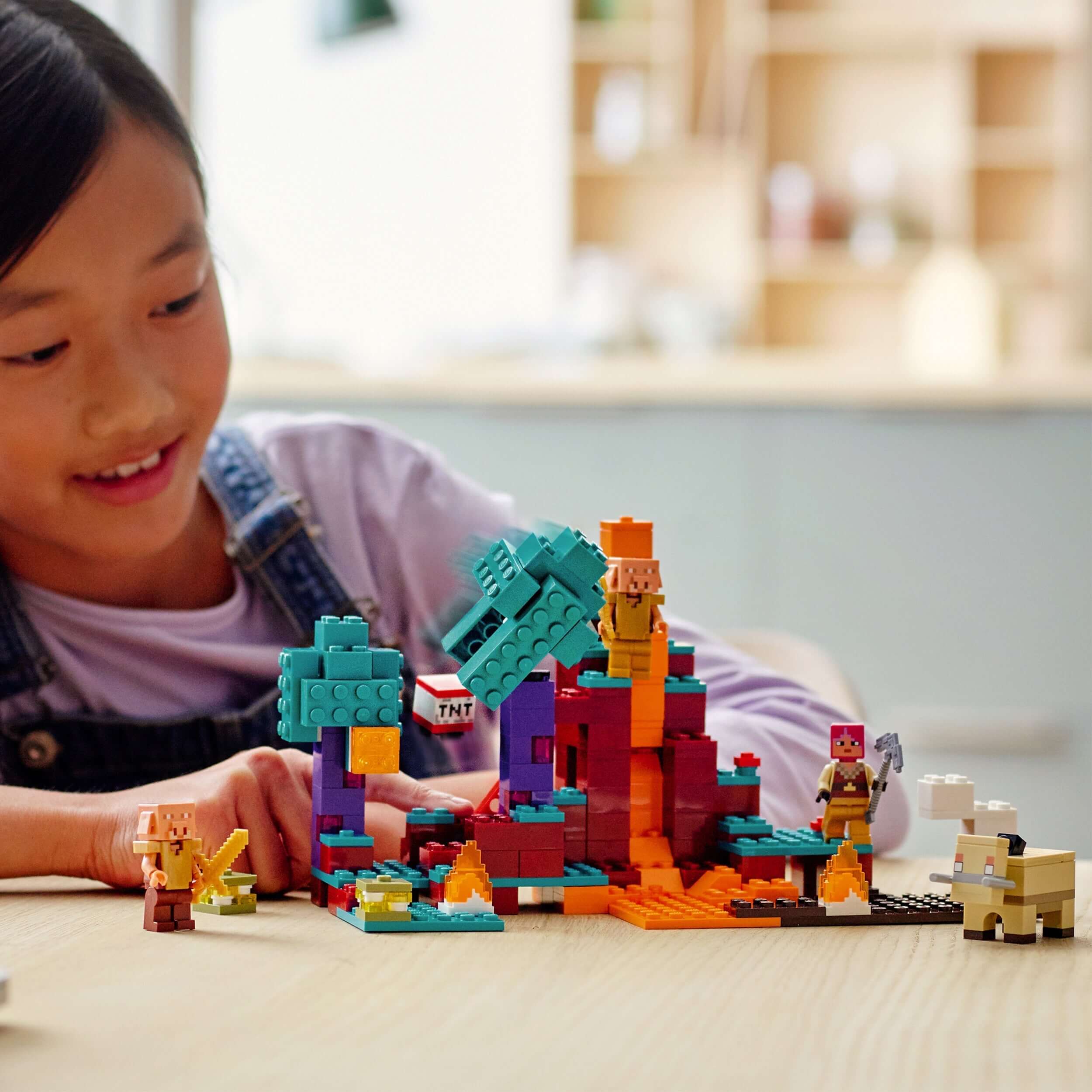 Child excitedly playing with LEGO® Minecraft 21168 set in a colorful warped forest setting.