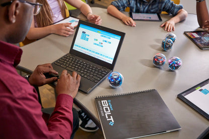 A student programming the Sphero BOLT+ robot on a laptop, with multiple BOLT+ robots and a guidebook on the table.