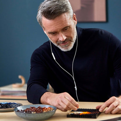 Adult man building LEGO® Art The Beatles set, enjoying immersive soundtrack, with colorful brick pieces and bowls on table.