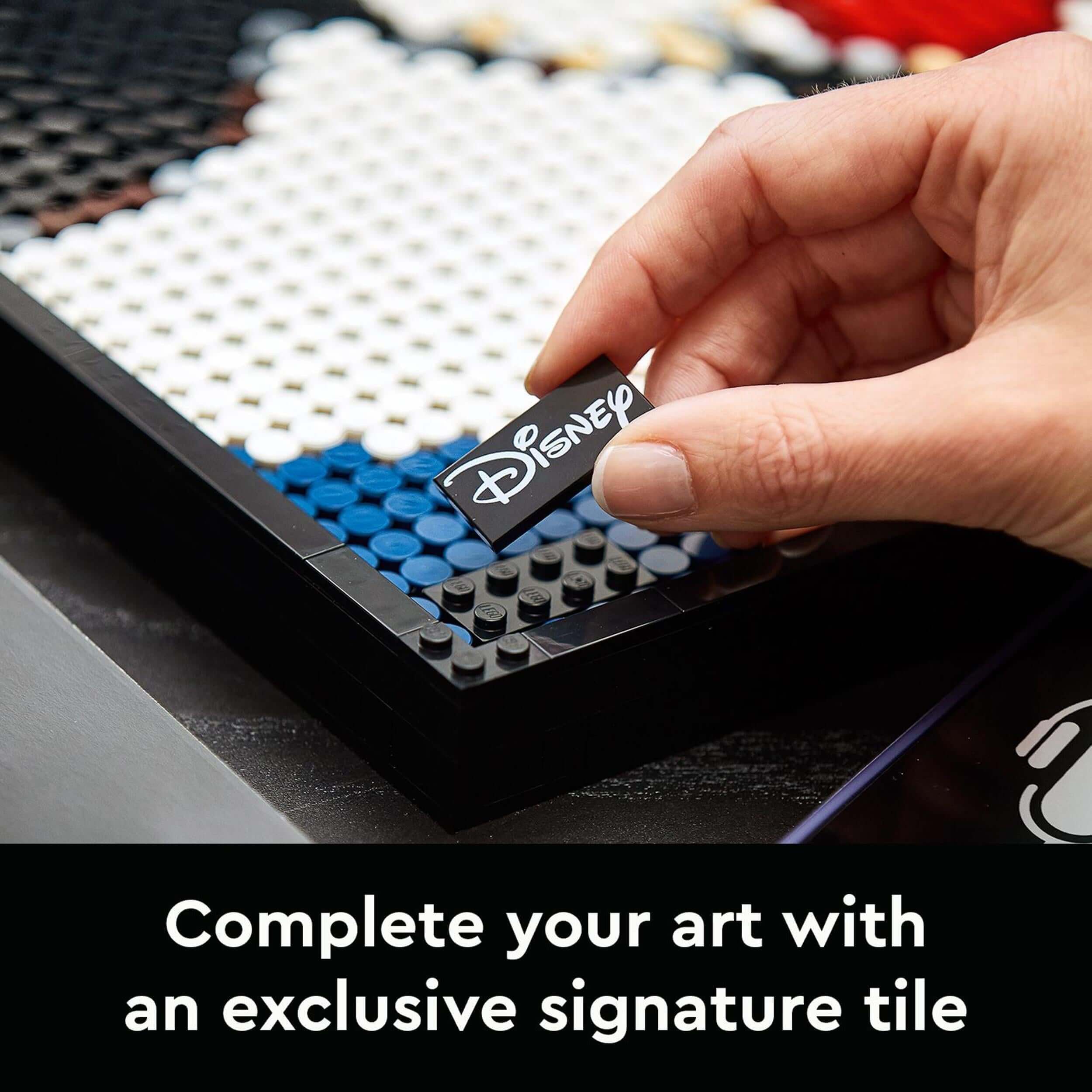 Hand placing a Disney signature tile in LEGO® Art Mickey Mouse Poster Set for a personalized touch.
