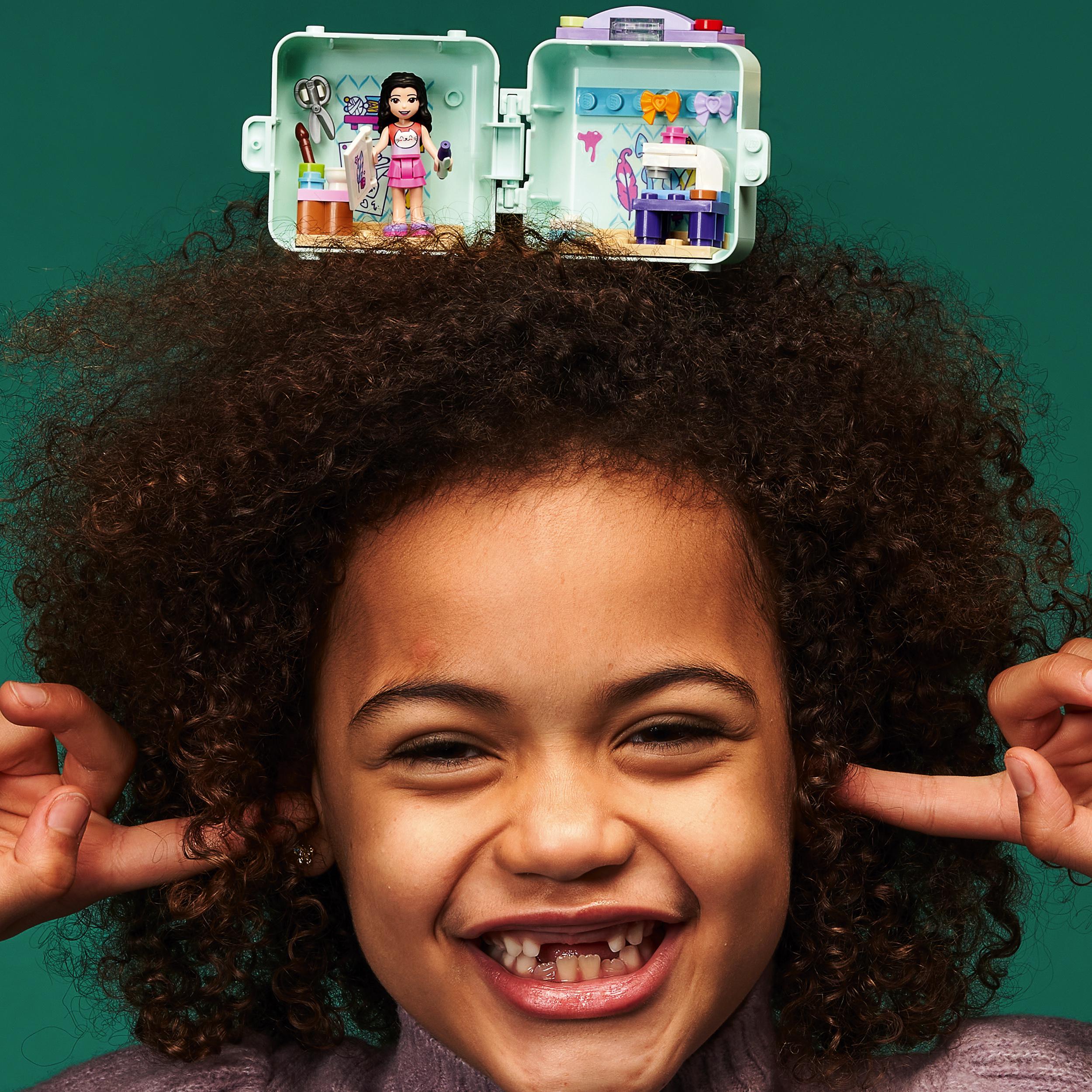 Girl smiling with LEGO® Friends Emma’s Fashion Cube Play Set on her head, showcasing creativity and fun.