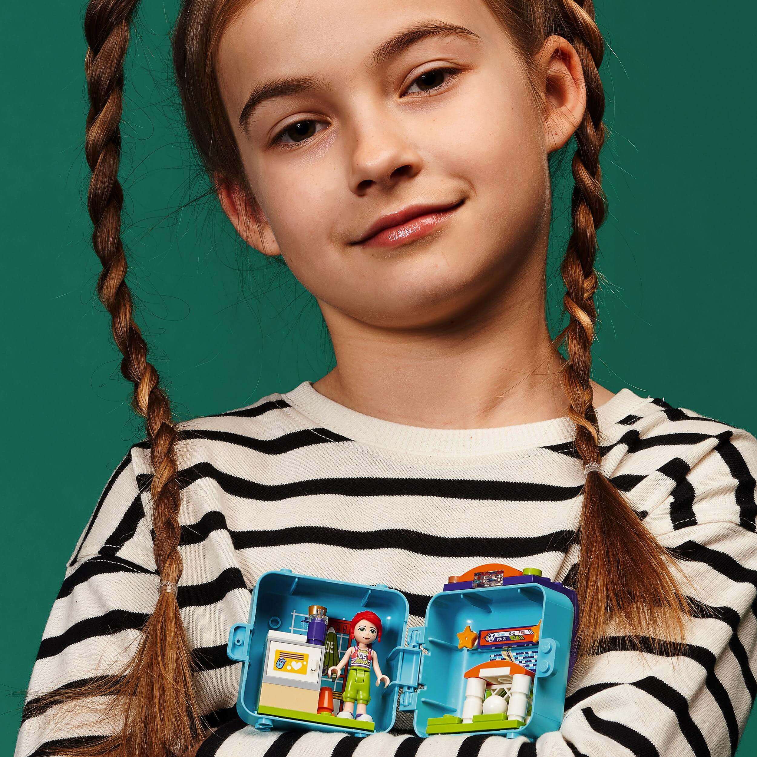 Girl showing LEGO® Friends Mia’s Soccer Cube playset, ideal for young football fans and travel. Portable play fun!
