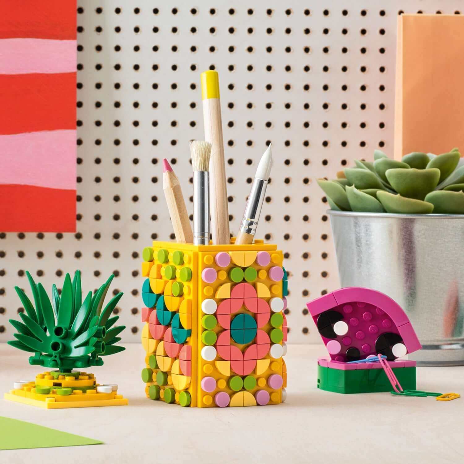 Colorful LEGO® DOTS Pineapple Pencil Holder with pens and pencils, set against a creative desk setup.