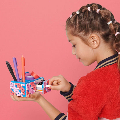 Girl organizing pens and craft supplies in a colorful LEGO® DOTS Desk Organiser on a pink background.