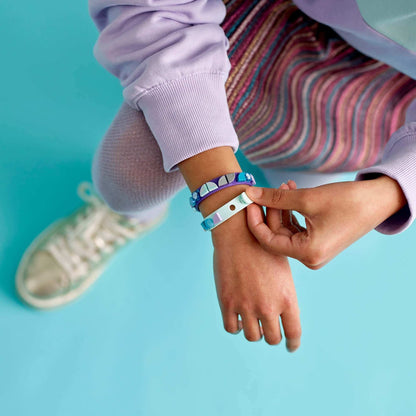 Child wearing LEGO® DOTS Mermaid Vibes Bracelets with colorful tiles on a blue background, showcasing creativity.