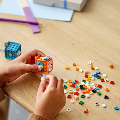 Child crafting with LEGO® DOTS tiles, assembling a colorful cube surrounded by various colorful pieces.