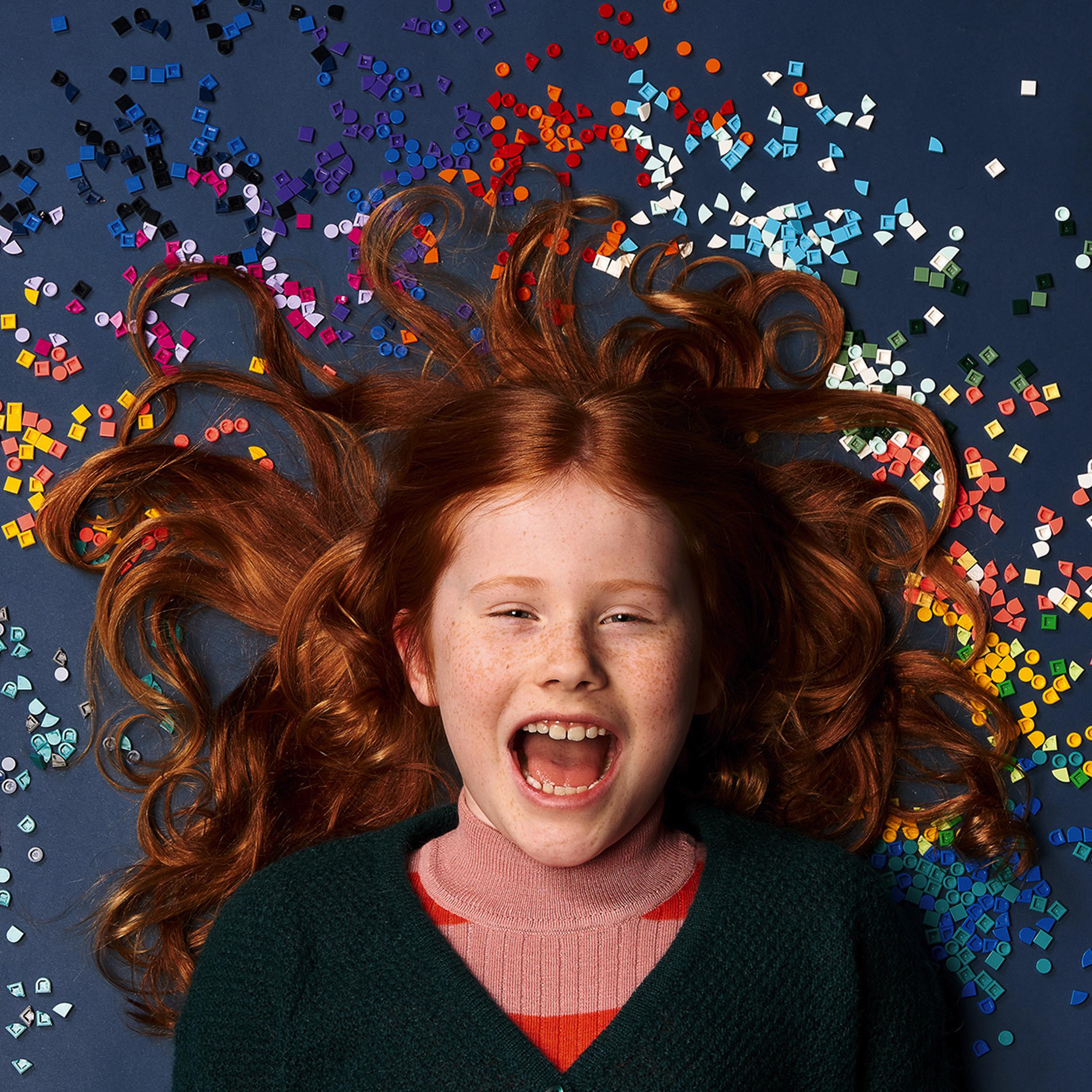 Child enjoying LEGO® DOTS tiles, surrounded by colorful craft pieces, showcasing creativity and fun.