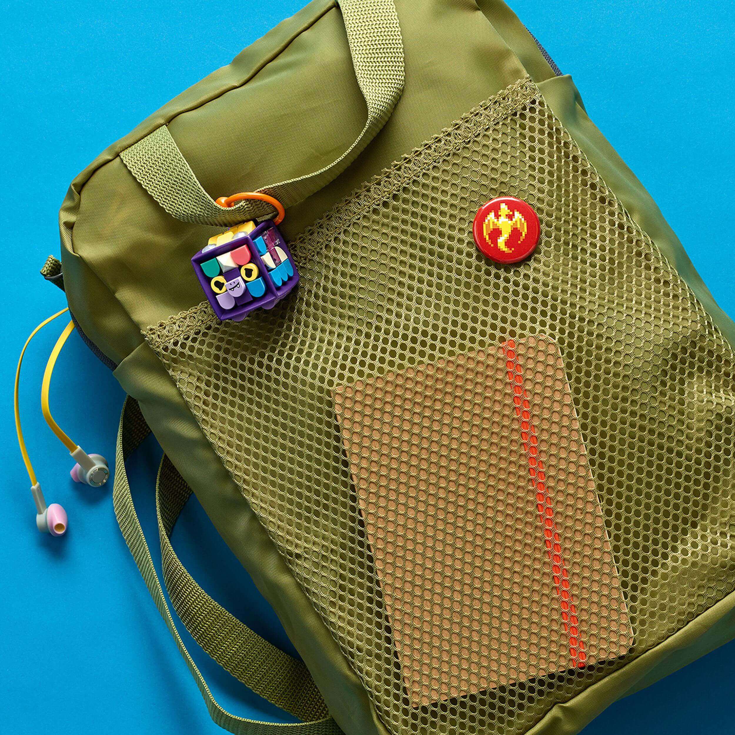LEGO® DOTS customizable bag tag dragon on a green backpack with notebook and earphones on a blue background.
