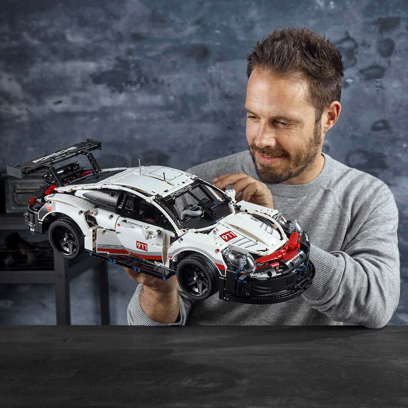 Adult holding LEGO® Technic Porsche 911 RSR model, showcasing realistic details like the working engine and suspension.