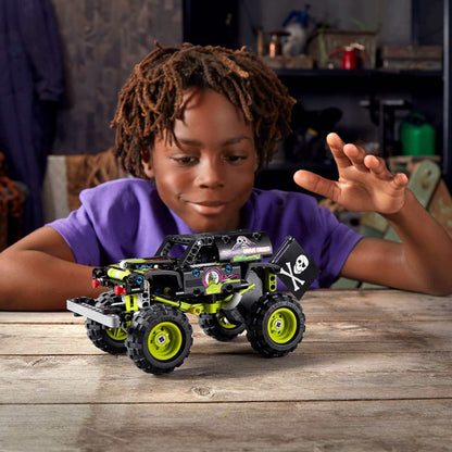 Child playing with LEGO® Technic Monster Jam Grave Digger Truck 42118 on a wooden table, showcasing creativity and fun.