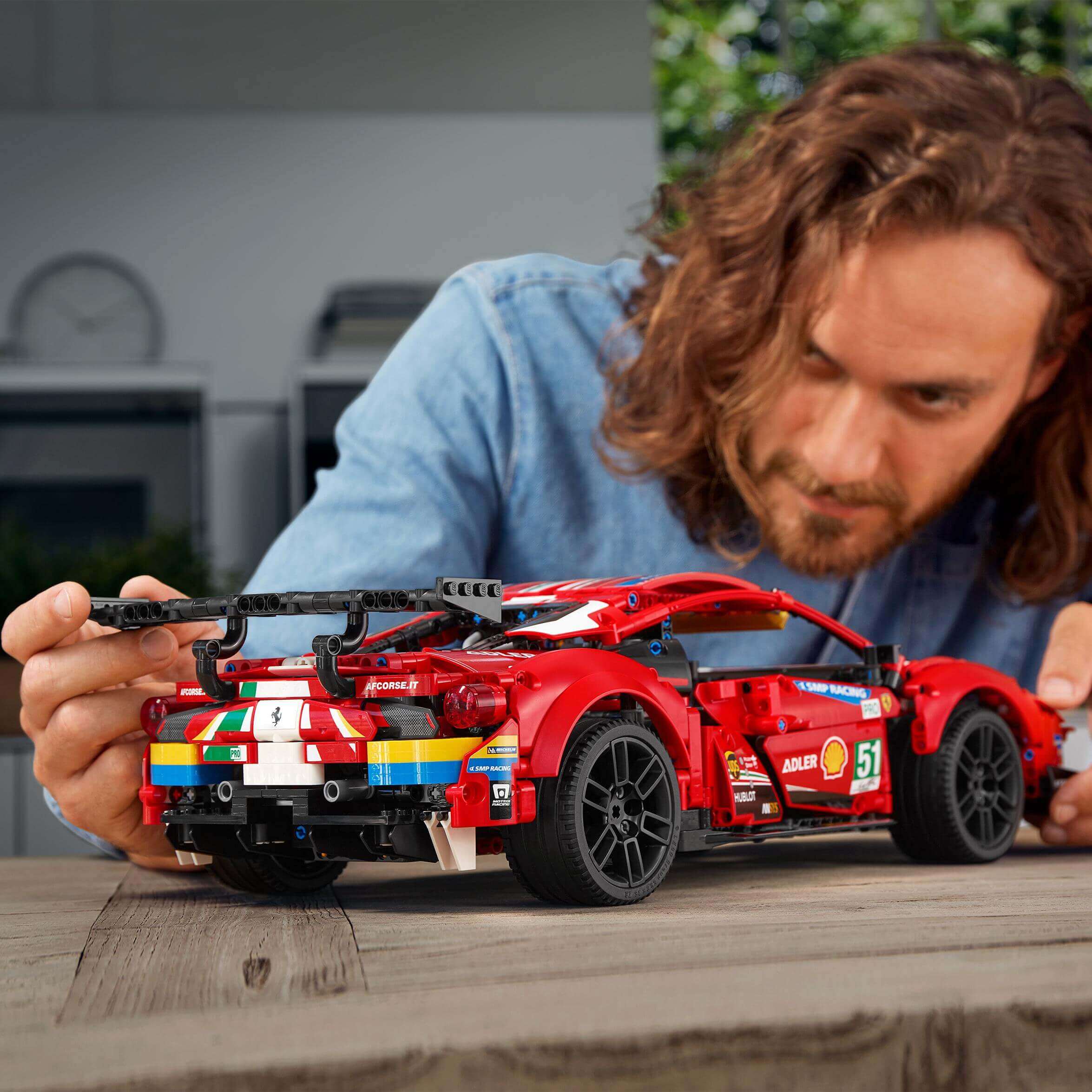 Person building a LEGO Technic Ferrari 488 GTE AF Corse #51 model, showcasing fine details in a home setting.
