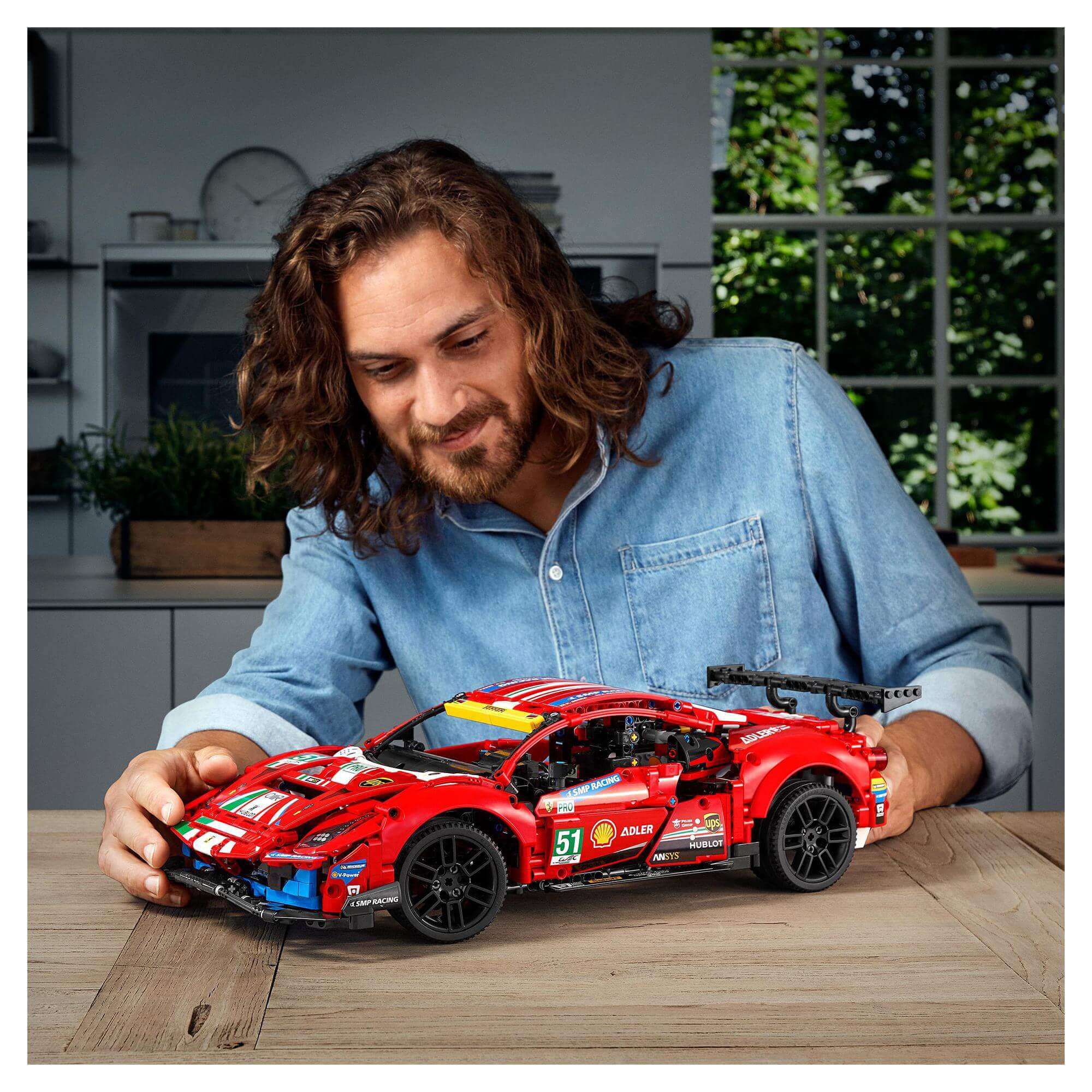 Person building LEGO Technic Ferrari 488 GTE AF Corse model on a table in a well-lit kitchen.
