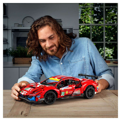 Person building LEGO Technic Ferrari 488 GTE AF Corse model on a table in a well-lit kitchen.