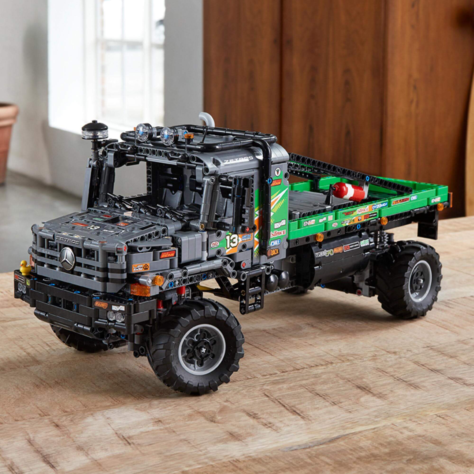 LEGO Technic 4x4 Mercedes-Benz Zetros Truck model on a wooden table, showcasing its detailed design and functionality.