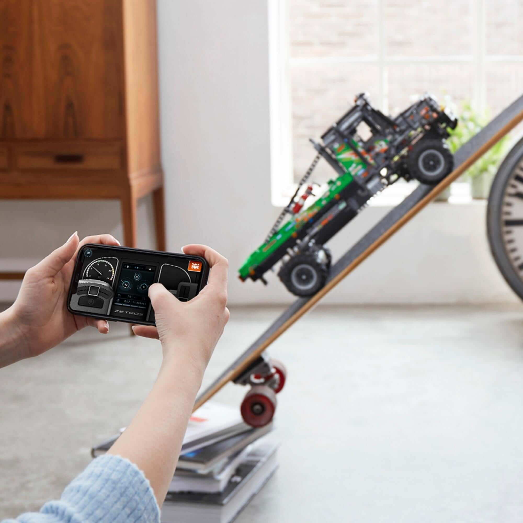 Child controlling LEGO® Technic 4x4 Mercedes-Benz Zetros Truck with CONTROL+ app on a smartphone.