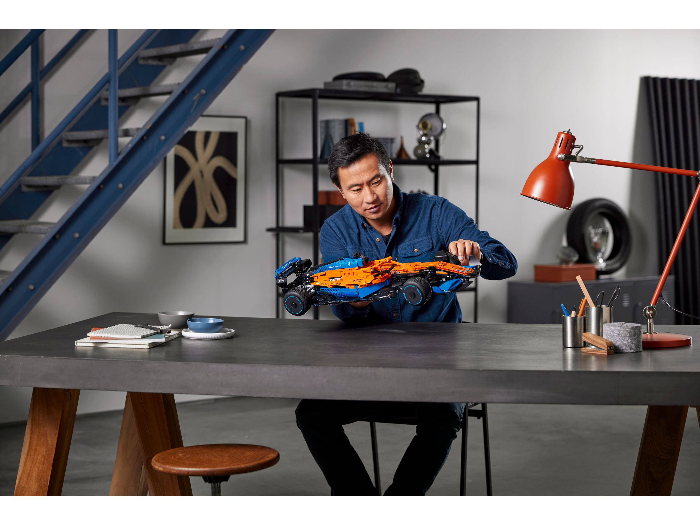 Person assembling LEGO Technic McLaren Formula 1 Race Car model at a modern desk with tools and decor.