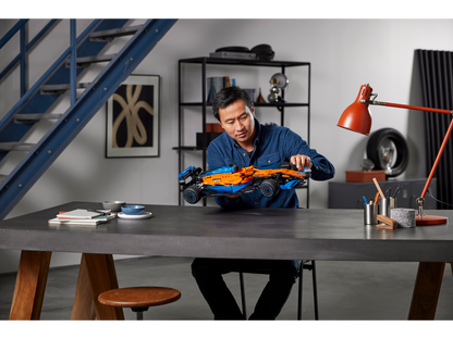 Person assembling LEGO Technic McLaren Formula 1 Race Car model at a modern desk with tools and decor.