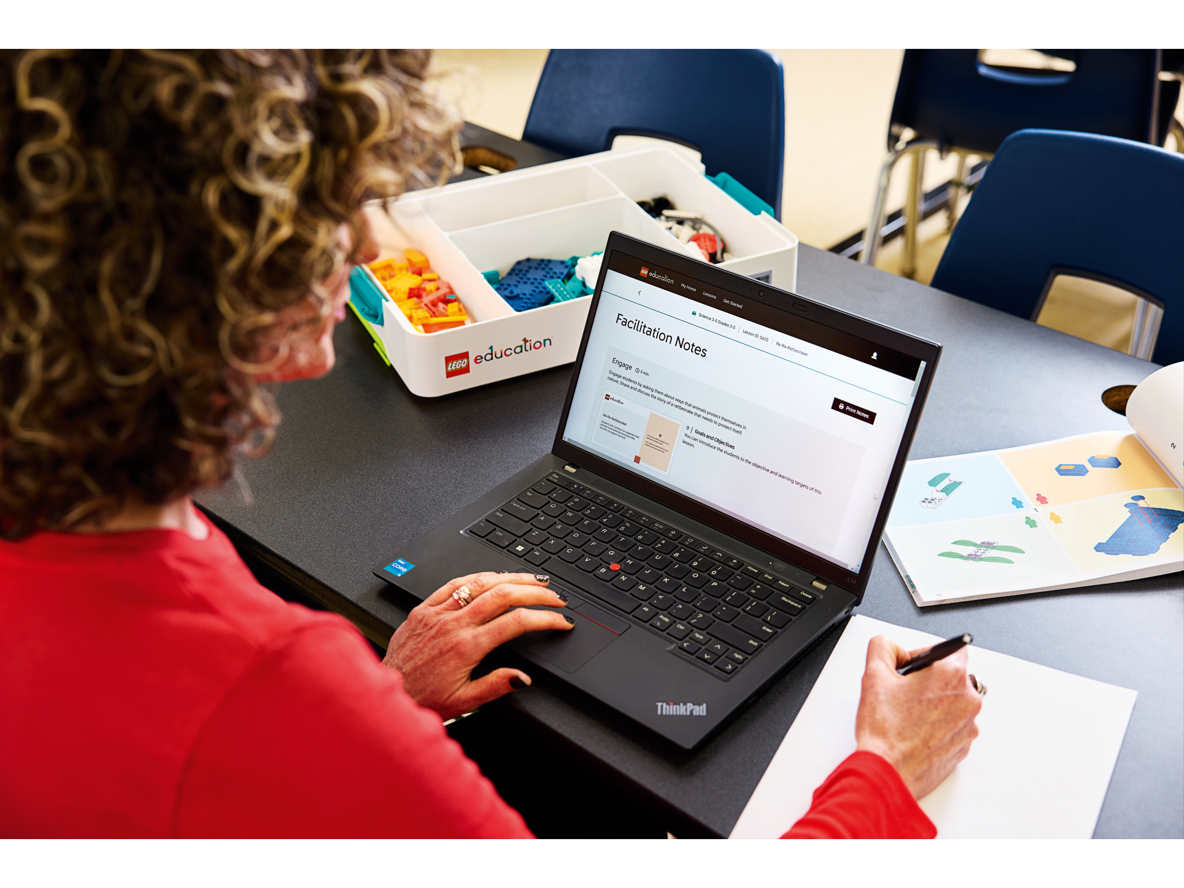 Person using a Lenovo ThinkPad laptop for educational facilitation notes in a classroom setting.