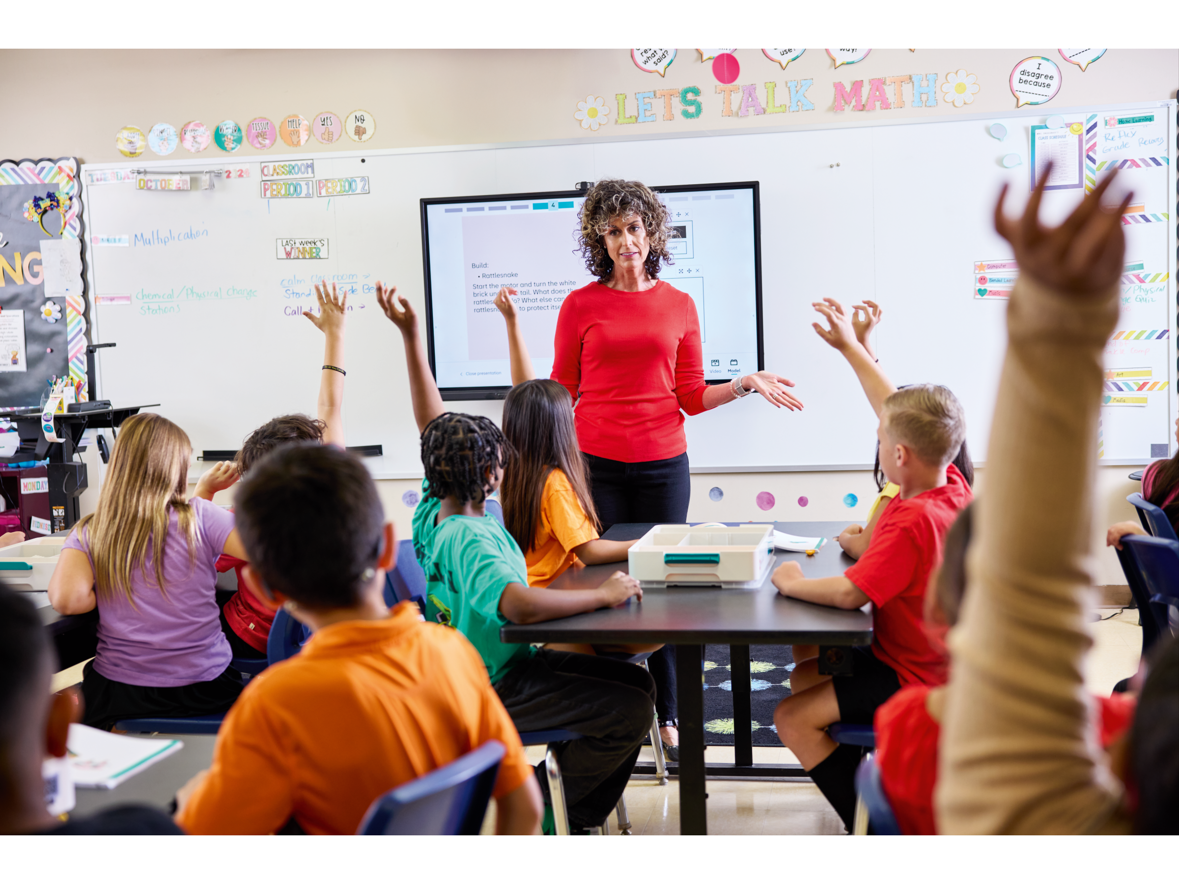 Teacher engaging students in a classroom discussion about math, children raising hands to participate.