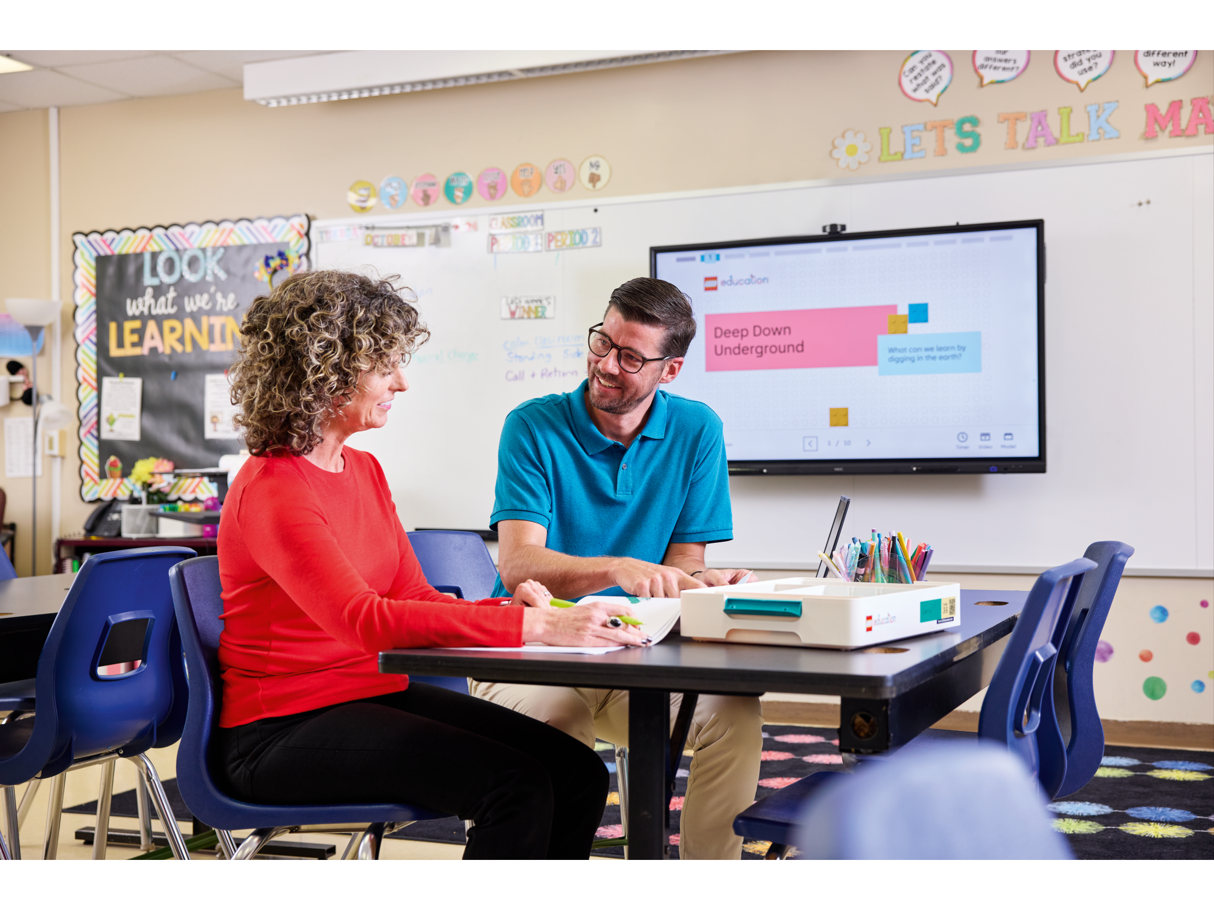 Teacher and student collaborating in a classroom, engaging in interactive learning with technology and materials.