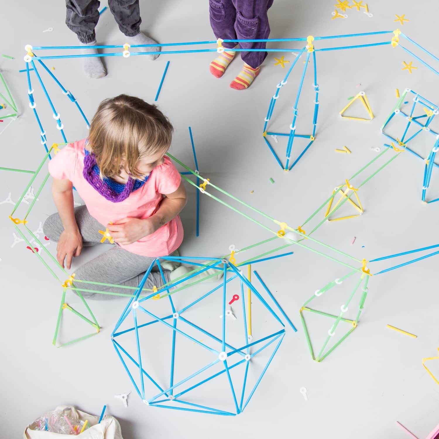 Children building creative structures with colorful straws from the Imagination Kit on a floor.