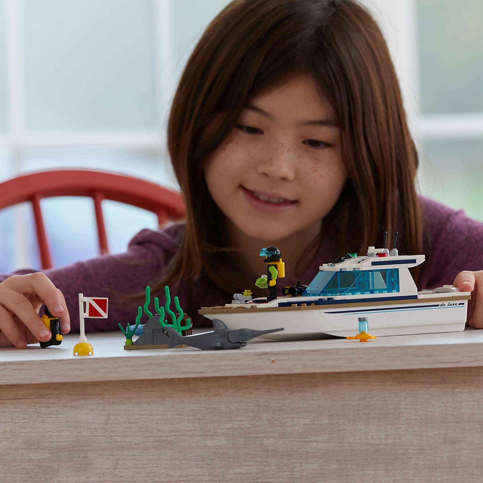 Child playing with LEGO® City Diving Yacht set 60221, exploring deep sea scenes with divers and marine life.