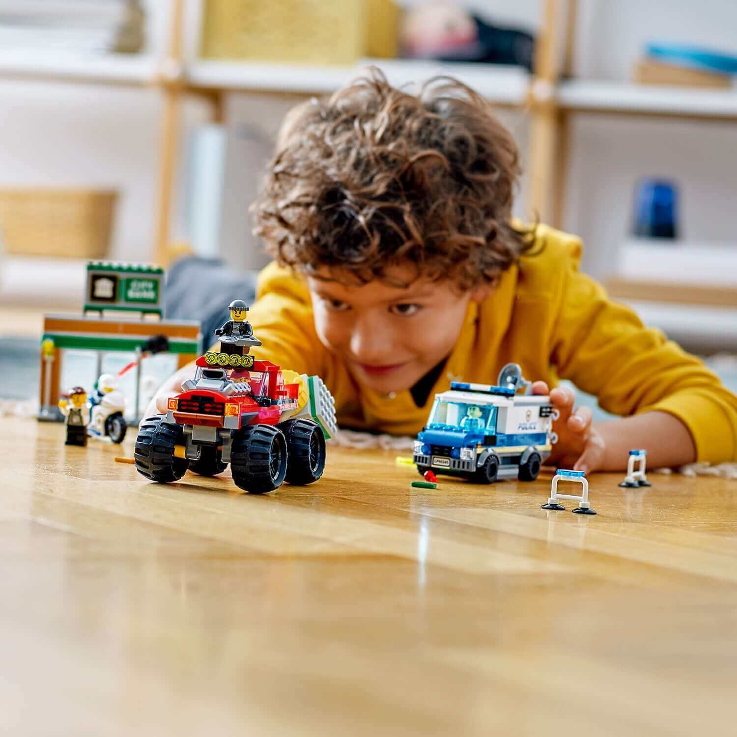 Child playing with LEGO® City Police Monster Truck Heist set, featuring a monster truck and police vehicles on the floor.