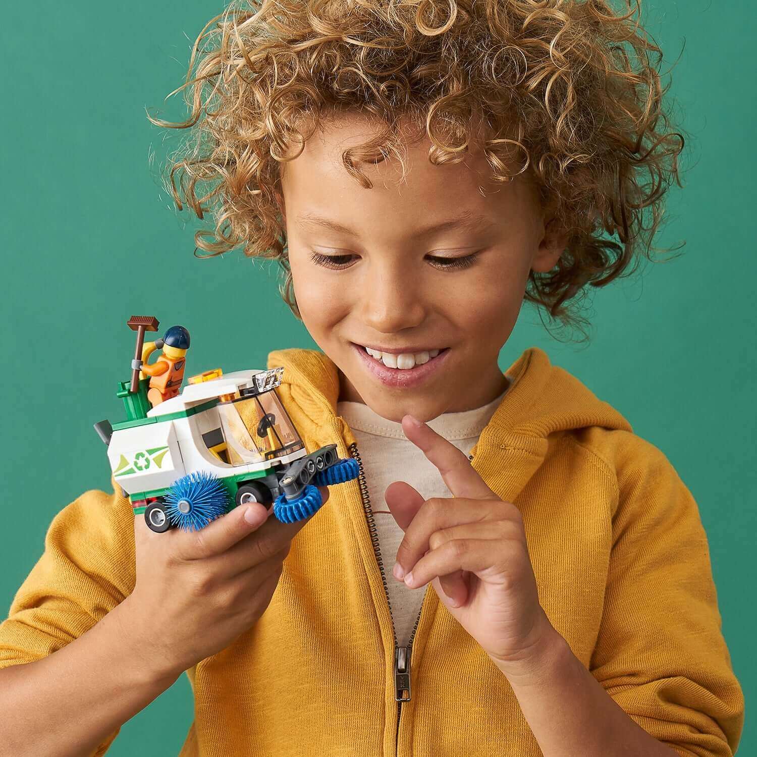 Child smiling while holding LEGO® City Great Vehicles Street Sweeper Toy 60249 with driver minifigure.