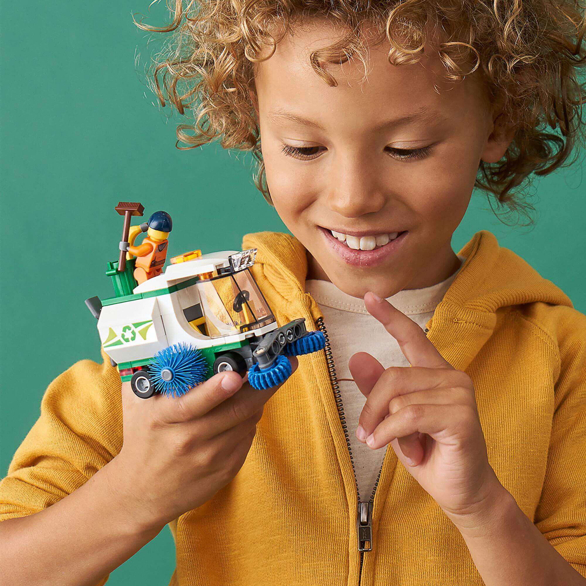 Child smiling while holding LEGO® City Street Sweeper Toy 60249 featuring a minifigure and spinning brushes.