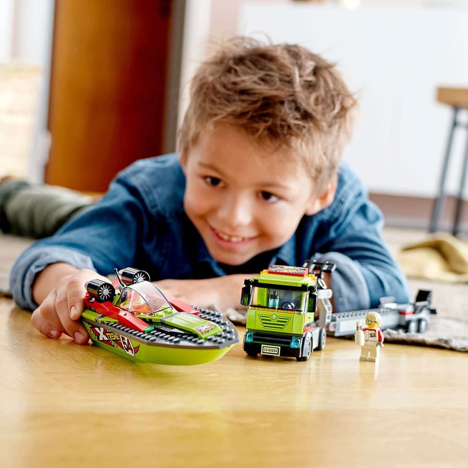 Child playing with LEGO City Race Boat Transporter 60254, featuring a speed boat and minifigures on a wooden floor.