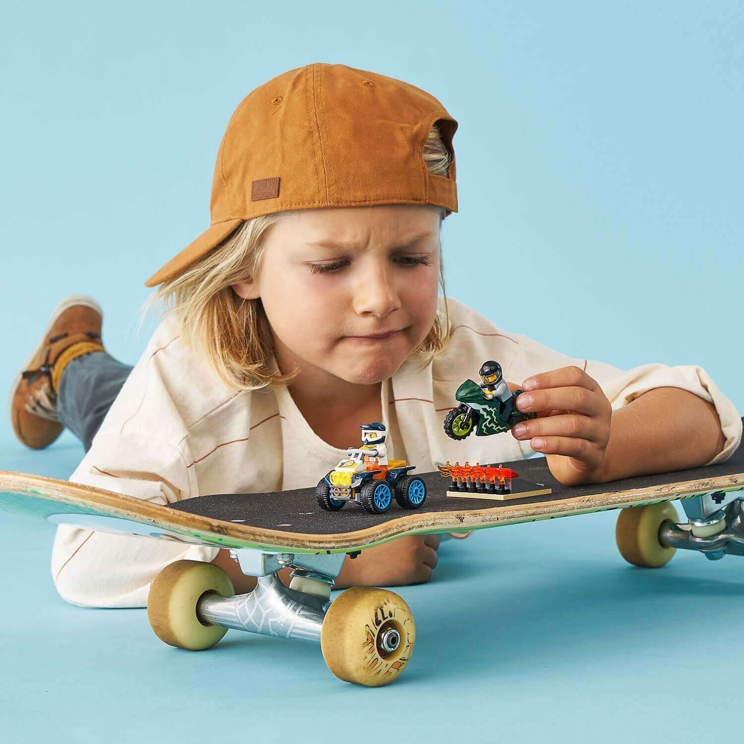 Child playing with LEGO® City Nitro Wheels Stunt Team set on a skateboard, featuring stunt ATV and motorcycle.