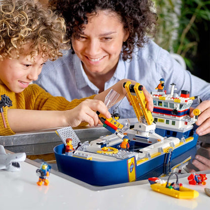 Child and parent enjoying LEGO® City Ocean Exploration Ship playset together, featuring marine figures and accessories.