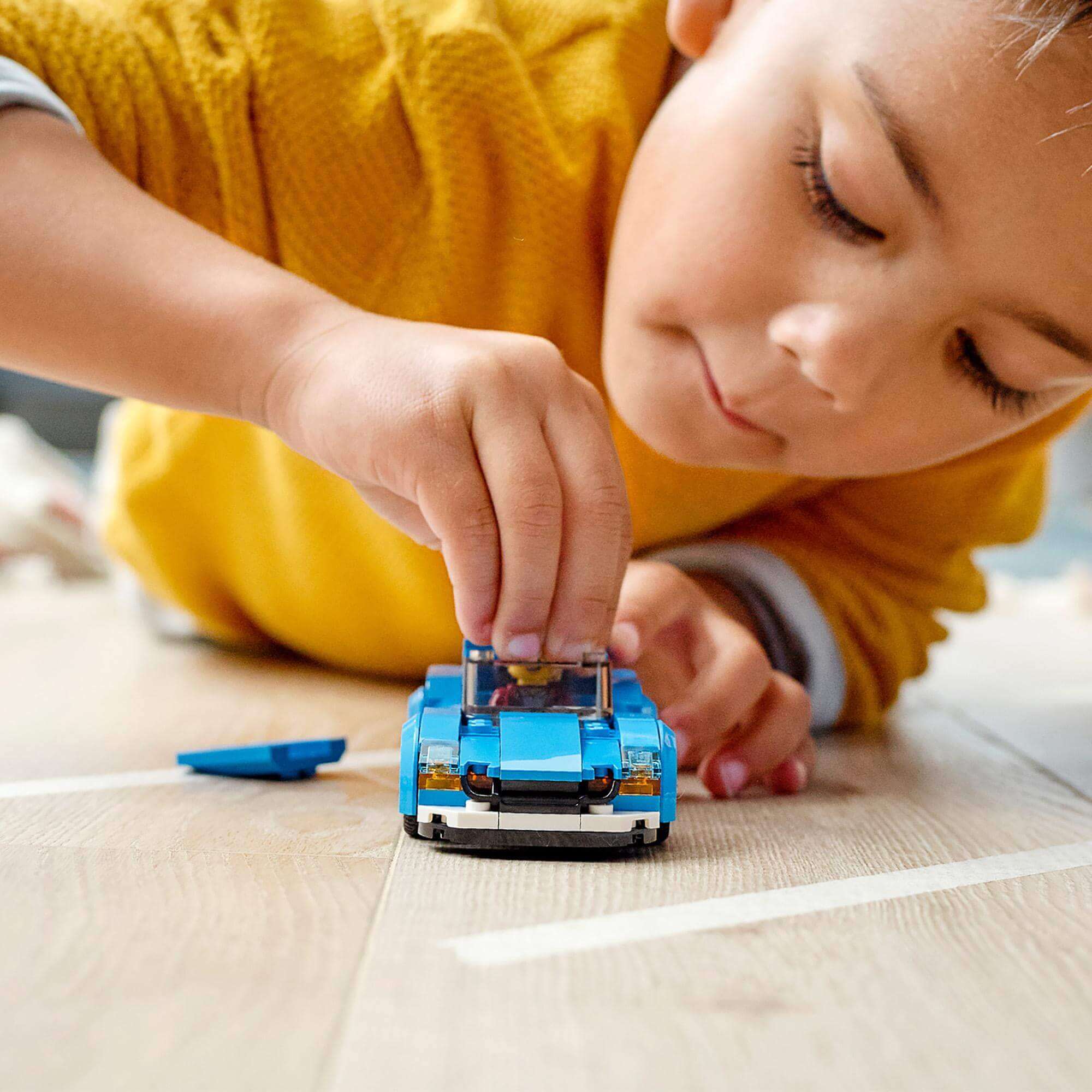 Child playing with LEGO® City Sports Car toy 60285, featuring a blue color and removable roof on the floor.